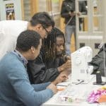 3 teens gather around a sewing machine